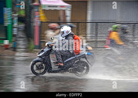 Imbevuto biker indonesiano a cavallo su scooter durante l acquazzone nella stagione delle piogge in Kota Bandung, West Java, Indonesia Foto Stock