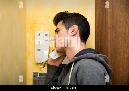 Giovane uomo rispondendo al citofono in un appartamento, ascoltando i suoi ospiti sull'altra estremità Foto Stock