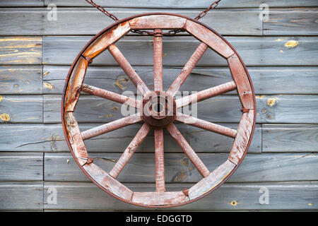 Vecchio usato ruota di legno appeso alla parete rurale sullo sfondo Foto Stock