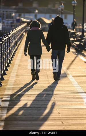 Il molo a Swanage nel Dorset. Un paio di piedi tenendo le mani al tramonto. Foto Stock