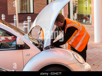 Meccanico maschio lavora su una macchina con il cofano (il cofano). Indossa un arancio hi-viz giacca. Scomodo concetto. Foto Stock