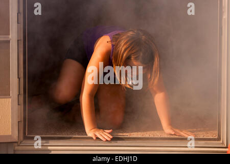 Una giovane ragazza che esce da un sopravvivere viva la costruzione di piene di fumo Foto Stock