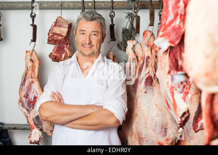 Macellaio in piedi con le braccia incrociate in macelleria Foto Stock