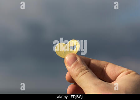 Una mano è in possesso di una bella luminosa forma di cuore con un piccolo cuore in esso, sullo sfondo del cielo con le nuvole. Foto Stock