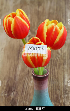 Scheda di merci (che significa grazie in francese) con rosso e tulipani gialli Foto Stock