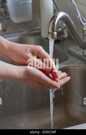 Chiudere fino a una giovane donna con le mani in mano essendo lavato in un metallo lavello da cucina Foto Stock