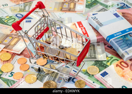 Carrello spesa piena di monete, in piedi sulle banconote in euro Foto Stock