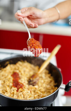 Donna di mettere la salsa di pomodoro in un tegame sul fornello Foto Stock