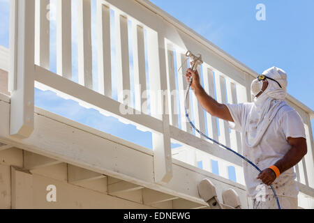 Pittore di casa indossando la protezione del viso verniciatura a spruzzo di un ponte di una casa. Foto Stock