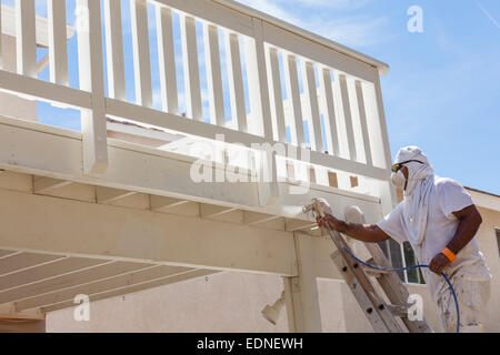 Pittore di casa indossando la protezione del viso verniciatura a spruzzo di un ponte di una casa. Foto Stock