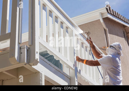 Pittore di casa indossando la protezione del viso verniciatura a spruzzo di un ponte di una casa. Foto Stock