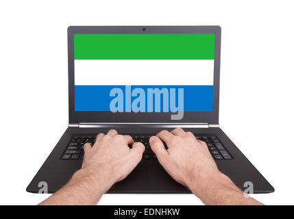 Mani lavorando su laptop che mostra sullo schermo la bandiera della Sierra Leone Foto Stock