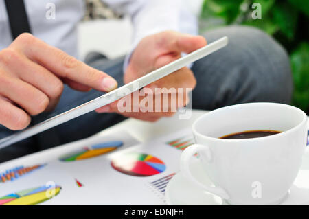 Primo piano di un giovane imprenditore utilizzando una compressa su un tavolo pieno di grafici Foto Stock