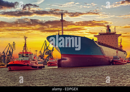 Grande nave con la scorta rimorchiatori partenza dal porto al tramonto. Foto Stock