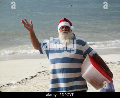 Anziano uomo vestito di Santa's hat sulla spiaggia del Mar dei Caraibi. Foto Stock