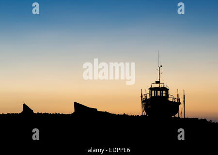 Barca da pesca sulla terraferma a sunrise nel porto di Lindisfarne, Isola Santa, Northumberland, Inghilterra. Silhouette Foto Stock