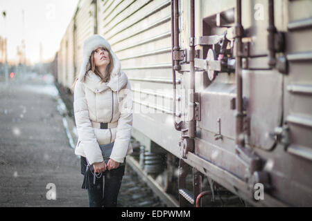 Giovane donna nel cappello di pelliccia e down jacket su una stazione ferroviaria Foto Stock