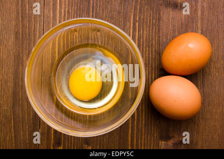 Aprire uovo sulla ciotola sul tavolo in legno visto da sopra Foto Stock
