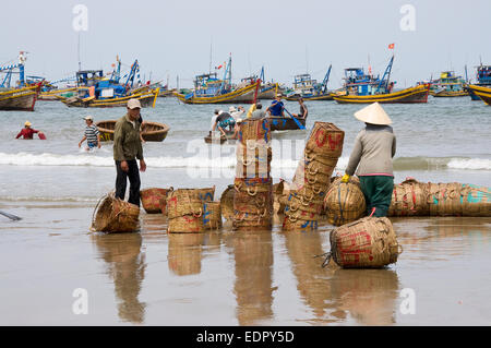 Lavorando pescatore cestini di impilamento in spiaggia nel sud del Vietnam Mui ne Foto Stock