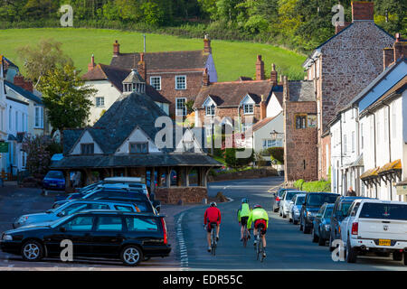 I ciclisti su una vacanza in bicicletta passato automobili parcheggiate attraverso la vecchia città di Dunster, nel Somerset, Regno Unito Foto Stock