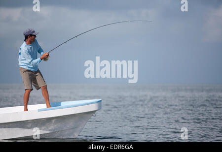 Fisherman sorge sulla prua della barca mentre la bobinatura in canna da mosca Foto Stock