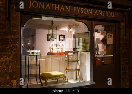 Mobili antichi nella finestra di visualizzazione al negozio di antiquariato lungo Burford High Street di notte, i Cotswolds Foto Stock