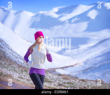 Il jogging all'aperto, carino donna sportive che corre lungo le montagne coperte di neve, allenamento nel periodo invernale, uno stile di vita attivo Foto Stock