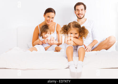 Famiglia seduta sul letto bianco in pigiama insieme Foto Stock