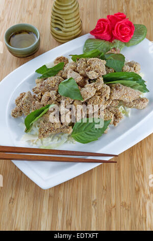 L'immagine verticale di cinesi affettato fritto di pollo cotto nel piatto bianco con tazza di ceramica e bere brocca in background sul naturale Foto Stock