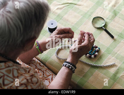 Donna anziana facendo collane in casa sua Foto Stock