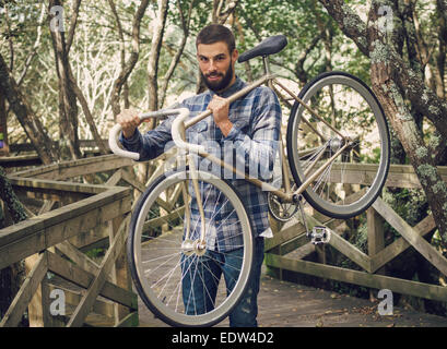 Hipster man tenendo la sua bicicletta in un parco all'aperto Foto Stock