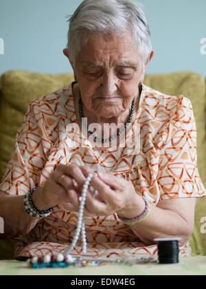 Donna anziana facendo collane in casa sua Foto Stock