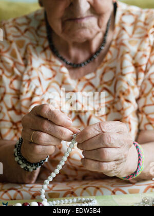 Donna anziana facendo collane in casa sua Foto Stock