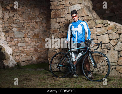 Ciclista in posa con la sua bici da corsa di fronte a un muro di pietra Foto Stock