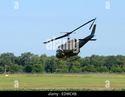 Il camuffamento verde elicottero militare UH-1 Huey volare al di sopra di un campo Foto Stock