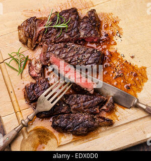 Grigliata di Ribeye con coltello e forchetta sulla carne tagliere su sfondo di legno Foto Stock