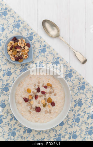 Una prima colazione di porridge di avena srved in una ciotola bianco su bianco sullo sfondo di legno. Foto Stock