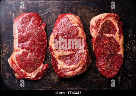 Tre tagli di materie fresche bistecche di carne e condimenti su sfondo scuro Foto Stock