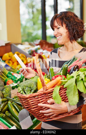 Donna sorridente con shopping list acquistare verdure fresche in un supermercato Foto Stock