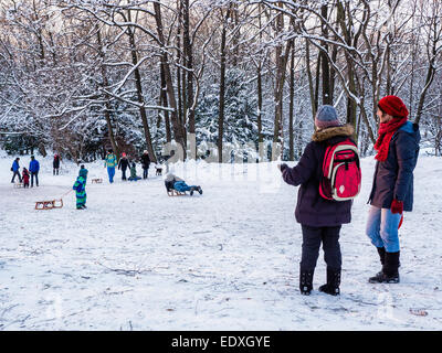 Due madri guardare i bambini lo slittino sulla coperta di neve pendio - parco pubblico in inverno, Humbolthain Volkspark, Brunnenviertel, Berlino Foto Stock