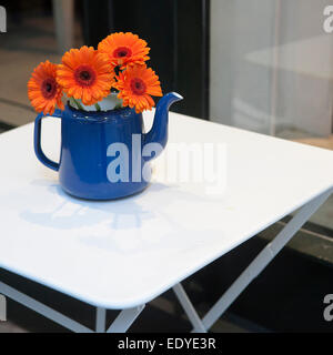 Orange gerbera fiore con gocce d'acqua in blu tè-vaso sul tavolo bianco come una decorazione della street cafe Foto Stock