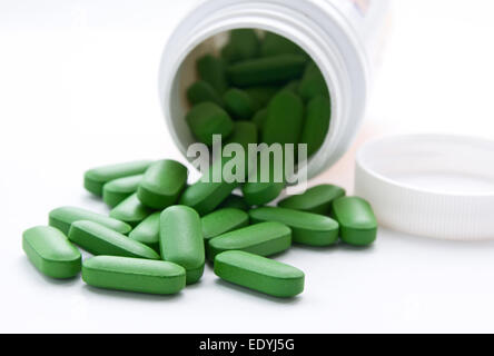 Queste sono multi-vitamina pillole. Le compresse di colore verde sono presi al di fuori della bottiglia bianca e situato su uno sfondo bianco. Foto Stock