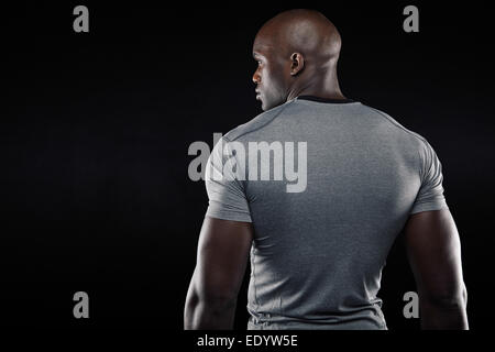 Vista posteriore di montare giovane con costituzione muscolare in piedi contro lo sfondo nero. Afro Americano modello di fitness in studio. Foto Stock