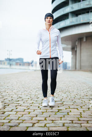 A piena lunghezza Ritratto di un bel giovane donna in sportswear esercizio all'esterno. Donna potenza a piedi sulla strada urbana. Foto Stock