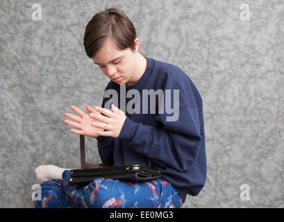 Ragazzo adolescente con autismo e sindrome di Down battendo le mani come suona con una compressa Foto Stock