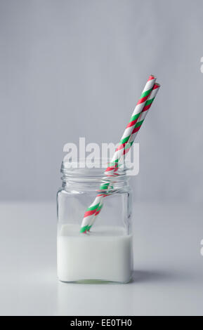 Latte in un vaso con un cannucce colorate su sfondo bianco, viola Foto Stock