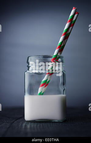 Latte in un vaso con un cannucce colorate su tavola nera Foto Stock