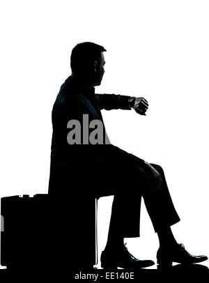 Un business caucasica uomo seduto sulla valigia controllo tempo silhouette a piena lunghezza in studio isolato su sfondo bianco Foto Stock