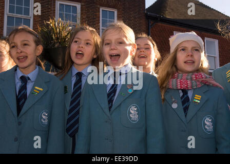 Gruppo di scolari a cantare i canti natalizi presso un esterno di mercato di natale, High St, Haslemere, Surrey, Regno Unito. Foto Stock