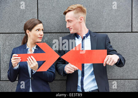 Business uomo e donna che mantiene due grandi frecce rosse contro ogni altro Foto Stock